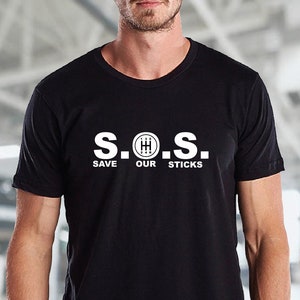 May include: A black t-shirt with a white graphic that says "S.O.S. SAVE OUR STICKS" with a stick shift gear symbol in place of the "O".