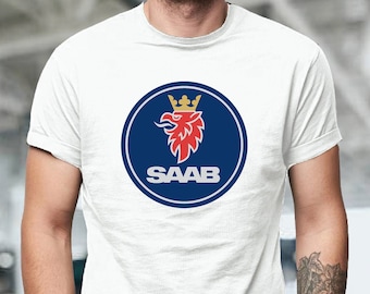 Op de afbeelding: Wit T-shirt met het Saab-logo. Het logo is een blauwe cirkel met een rode griffioen en een gouden kroon, en het woord "SAAB" in het wit. Het shirt heeft korte mouwen en wordt door een persoon gedragen.