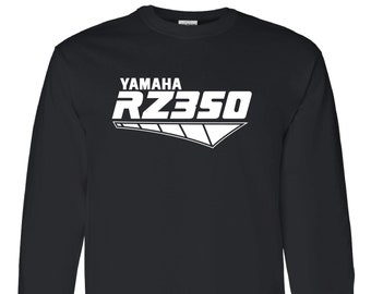 Op de afbeelding: Zwart shirt met lange mouwen met de witte tekst "YAMAHA RZ350" in een gestileerd lettertype. Het shirt heeft een grafisch ontwerp met een witte hoekige vorm onder de tekst. Het shirt is gemaakt van zacht materiaal.