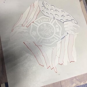 K&ouml;nnte beinhalten: Eine wei&szlig;e Schablone einer amerikanischen Flagge mit rotem Umriss, an den R&auml;ndern zerrissen, die ein Feuerwehr-Emblem mit dem Text "FARLEY FIRE EMS" in der Mitte freilegt.