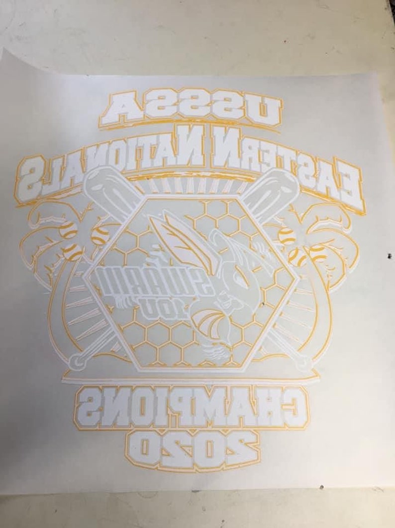 K&ouml;nnte beinhalten: Wei&szlig;er Text auf gelbem Hintergrund lautet "Eastern National 2020 Champions". Eine wei&szlig;e Biene mit Fl&uuml;geln befindet sich in der Mitte eines Sechsecks mit einem Wabenmuster. Die Biene h&auml;lt in jeder Hand einen Baseballschl&auml;ger. An beiden Seiten des Sechsecks befinden sich Palmen.