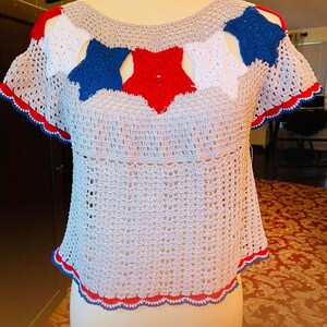 May include: A crocheted top with a red, white, and blue star design. The top has a scalloped hem and short sleeves.