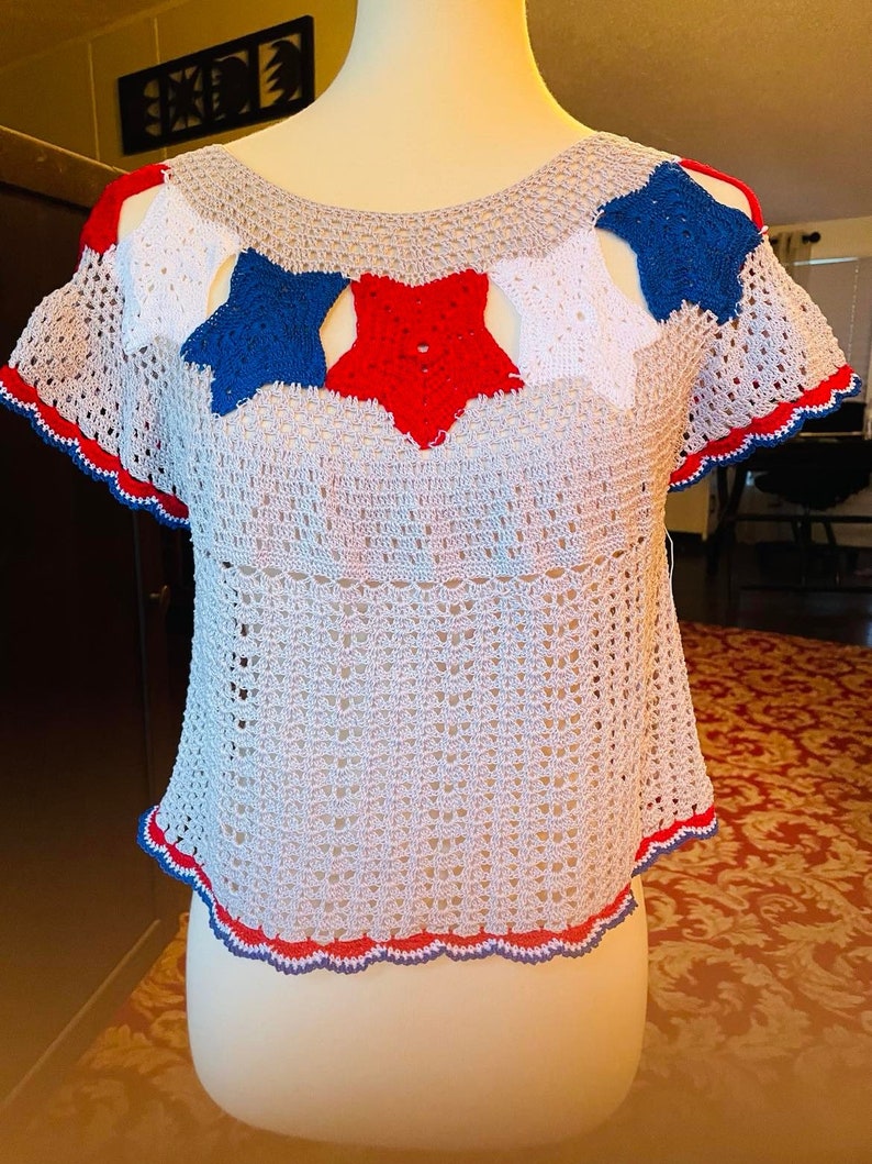 May include: A crocheted top with a red, white, and blue star design. The top has a scalloped hem and short sleeves.