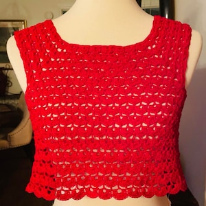 May include: A bright red, sleeveless crochet top. The top has a scoop neckline and a scalloped hem. The crochet pattern creates an open, airy design. The garment is displayed on a mannequin.