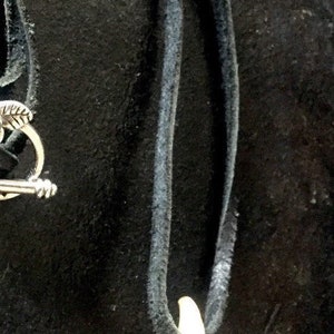 May include: A black leather cord necklace with a silver clasp and a white tooth pendant.