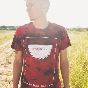 May include: A red and black tie-dye t-shirt with a white graphic of a saw blade and the text "REFORMATION" and "SAN ANGELO, TEXAS".