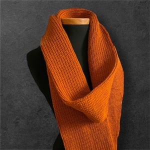 May include: A warm orange knitted scarf, folded and displayed on a mannequin.