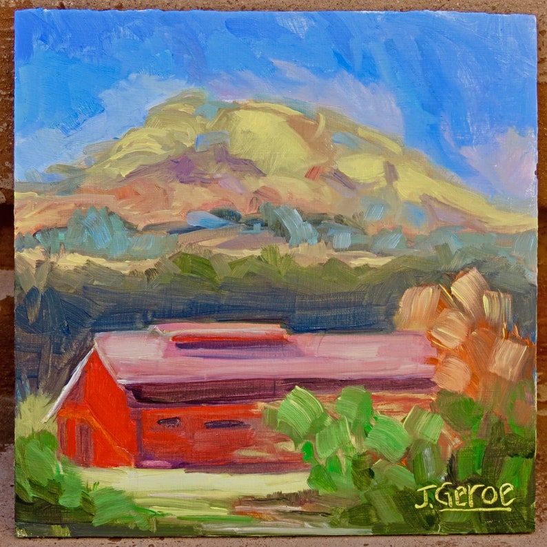 May include: A painting of a red barn with a pink roof in front of a green hill and blue sky. The hill is yellow and brown in the distance. The painting is signed "J. Geroe" in the bottom right corner.