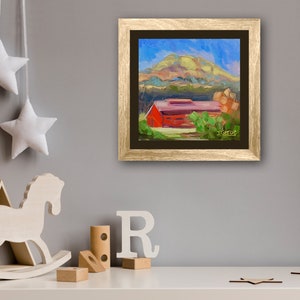 May include: A framed painting of a red barn with a green roof, surrounded by trees and a hill in the background. The sky is blue with white clouds. The painting is in a gold frame.