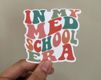 May include: A white sticker with the text "In My Med School Era" in colorful, retro-style lettering. The letters are in shades of red, orange, green, and pink.
