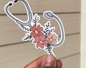 May include: A white sticker with a gray stethoscope and pink flowers. The stethoscope is in the shape of a heart.