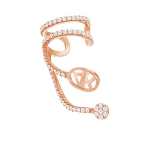Puede incluir: Un pendiente de aro de oro rosa con una triple fila de diamantes pavé y un pequeño racimo de diamantes en el extremo. El pendiente de aro tiene un pequeño dije ovalado con las letras "VK" en una fuente de escritura.