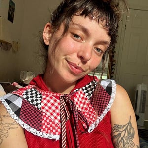 May include: A red sleeveless top featuring a wide, detachable collar made of patchwork fabric in red and white gingham, black and white checkered patterns, and red and black checkered squares, finished with a delicate white lace trim edge.