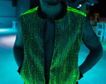 May include: A person wearing a green, light-up vest with a zipper. The vest is made of a fabric with many small, green lights. The person is standing in a dark room with blue lighting.