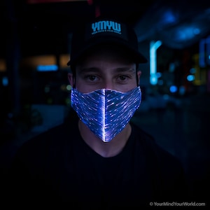 May include: A person wearing a black t-shirt and a black baseball cap with the text "YMYW Your Mind Your World" in white. The person is wearing a blue light-up face mask.