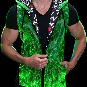 Puede incluir: Un chaleco verde con capucha, cremallera negra y forro estampado en blanco y negro. El chaleco está hecho de un material que se ilumina con luces verdes.