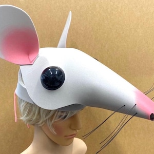 Peut inclure: Un masque de souris blanc doté de grandes oreilles arrondies avec des centres aérographes roses, un long museau à pointe rose, de fines moustaches en fil noir et un grand œil circulaire noir brillant. Le masque est fait de mousse lisse et légère.