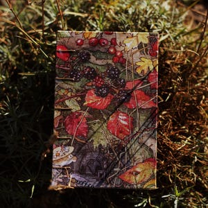 May include: A vintage-style fabric journal cover with a colourful floral and berry pattern. The cover features red, green, yellow, and brown colours. The journal cover has a textured surface.