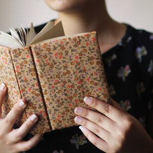 Puede incluir: Un libro abierto con una cubierta estampada floral en tonos beige, rojo y morado. Las p&aacute;ginas del libro son visibles, y el lomo es de un beige m&aacute;s oscuro. El libro est&aacute; abierto.