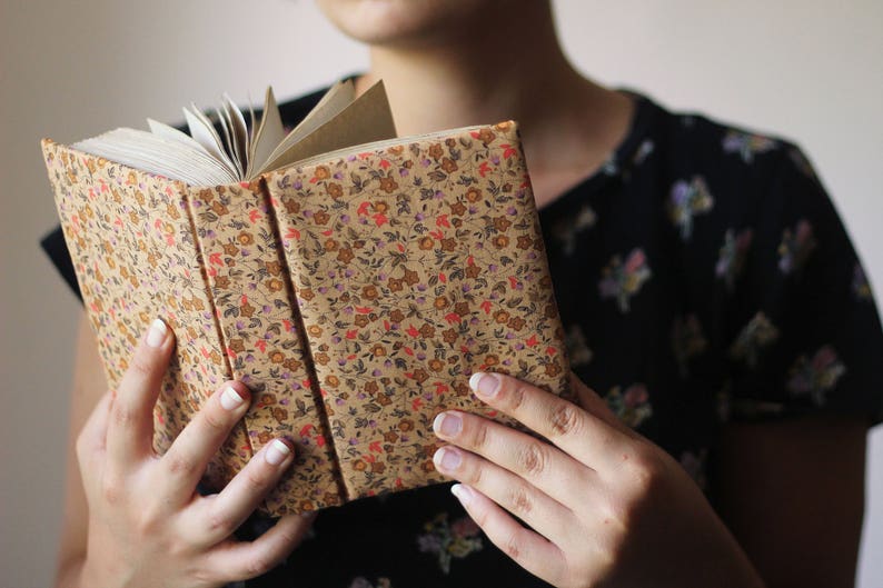 Puede incluir: Un libro abierto con una cubierta estampada floral en tonos beige, rojo y morado. Las p&aacute;ginas del libro son visibles, y el lomo es de un beige m&aacute;s oscuro. El libro est&aacute; abierto.