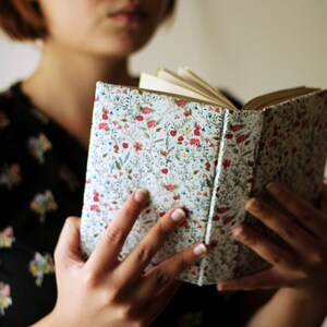May include: An open book with a floral patterned cover. The cover features a white background with a repeating pattern of red, blue, and green flowers and leaves. The book's pages are visible and appear to be aged.