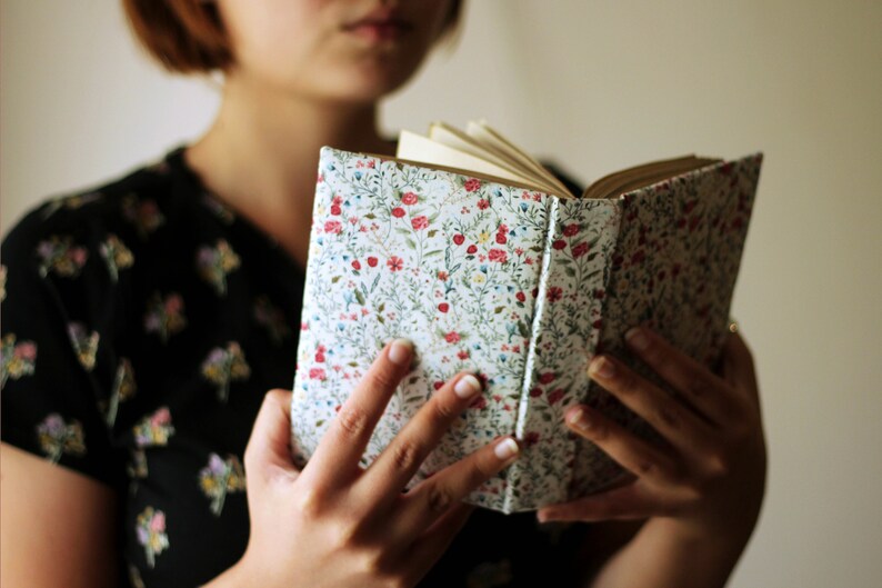 May include: An open book with a floral patterned cover. The cover features a white background with a repeating pattern of red, blue, and green flowers and leaves. The book's pages are visible and appear to be aged.