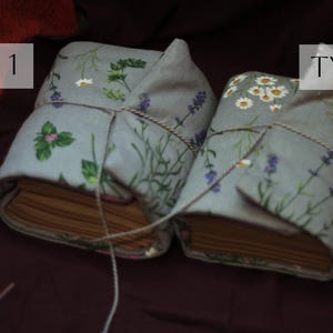 May include: Two fabric-covered books tied with twine. The covers are light blue with floral patterns, including herbs, lavender, and daisies. The text "TYPE 1" and "TYPE 2" are in white boxes on the top of the books.