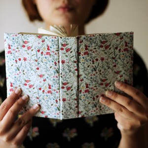 May include: An open book with a floral pattern cover. The cover features a white background with a repeating pattern of red, blue, and green flowers and leaves. The pages are visible.