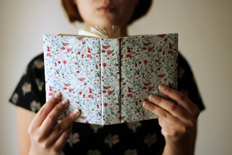 May include: An open book with a floral pattern cover. The cover features a white background with a repeating pattern of red, blue, and green flowers and leaves. The pages are visible.
