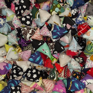 May include: A large collection of small, pyramid-shaped fabric pouches featuring a wide variety of colorful patterns, including floral, geometric, animal prints, and text-based designs in shades of red, blue, green, black, white, and pink.