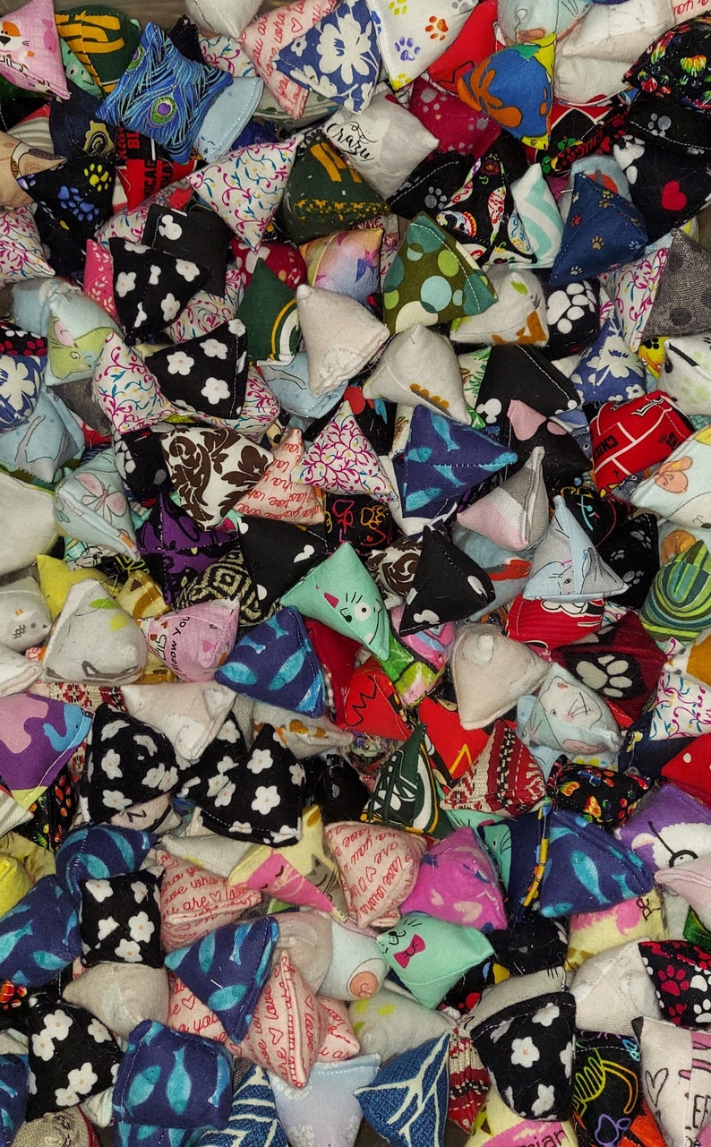 May include: A large collection of small, pyramid-shaped fabric pouches featuring a wide variety of colorful patterns, including floral, geometric, animal prints, and text-based designs in shades of red, blue, green, black, white, and pink.