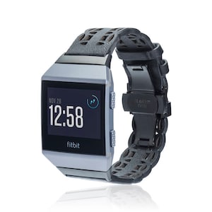 Puede incluir: Un reloj inteligente Fitbit plateado con una correa de cuero negra. La esfera del reloj muestra la fecha "NOV 28" y la hora "12:58".