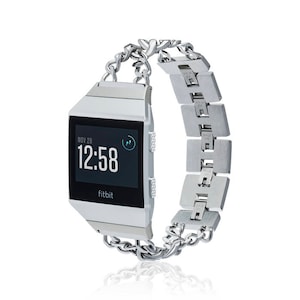 Puede incluir: Pulsera de reloj de eslabones de cadena plateada para un reloj inteligente Fitbit. La pulsera está hecha de metal y tiene un acabado plateado. La esfera del reloj muestra la fecha, la hora y un pequeño icono.