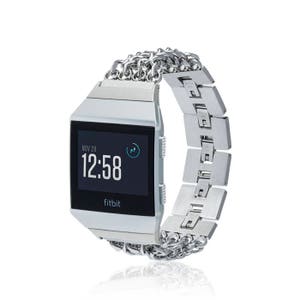 Puede incluir: Reloj inteligente Fitbit plateado con una banda de eslabones de cadena plateada. La esfera del reloj muestra la fecha, la hora y un pequeño icono. El texto "fitbit" se muestra en la esfera del reloj.