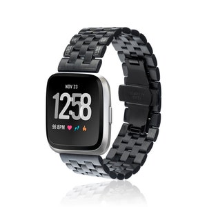 May include: Black metal band for a smartwatch with a black face displaying the date, time, and heart rate. The band has a stainless steel clasp.