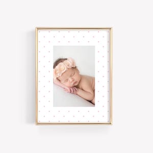 May include: A gold-colored picture frame with a white background and a pink polka dot pattern. The frame contains a photo of a baby sleeping with a flower crown on their head.