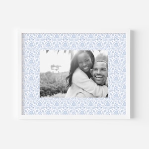 May include: A black and white photo of a couple smiling. The woman is wearing a white sweater and has her arm around the man. The man is wearing a white shirt and has his arm around the woman's waist. The photo is framed in a white frame with a blue and white patterned border.