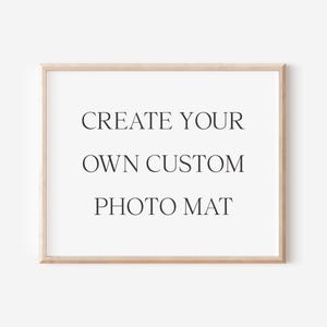 May include: A rectangular light wood picture frame containing a white mat board with the black text CREATE YOUR OWN CUSTOM PHOTO MAT centered in the middle. The frame has a simple, clean edge and a natural wood grain finish surrounding the white space.