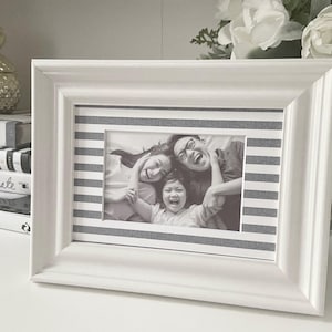 May include: A white picture frame with a black and white striped mat. The frame contains a black and white photo of a family of three. The photo shows a man, a woman, and a child.