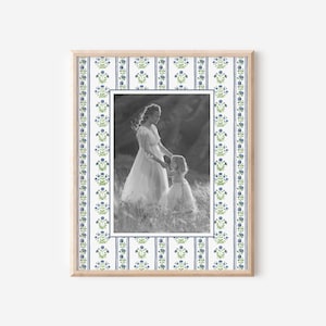 May include: A black and white photo of a mother and daughter in a frame with a blue and green floral pattern. The mother is wearing a long dress and holding the daughter's hand. The daughter is wearing a dress and looking at the camera.