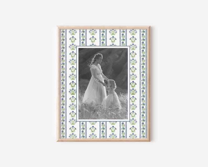 May include: A black and white photo of a mother and daughter in a frame with a blue and green floral pattern. The mother is wearing a long dress and holding the daughter's hand. The daughter is wearing a dress and looking at the camera.
