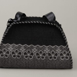 以下が含まれることがあります： グレーの刺繍模様が施された黒いハンドバッグ。バッグには黒い革のハンドルが2つ付いています。