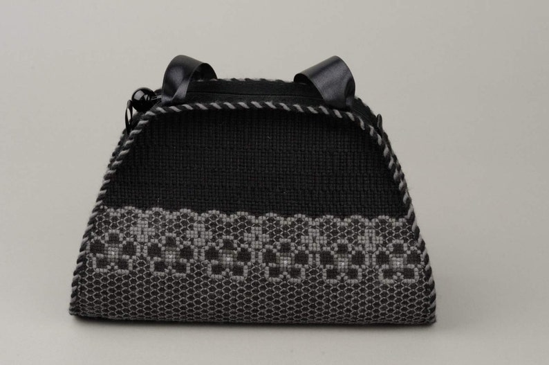 以下が含まれることがあります： グレーの刺繍模様が施された黒いハンドバッグ。バッグには黒い革のハンドルが2つ付いています。