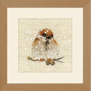May include: A framed cross-stitch artwork featuring two birds perched on a branch, with a backdrop of falling snow. The birds have brown and white plumage, and the artwork is set against a beige background. The frame is a light brown color.