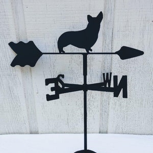 May include: Black metal weather vane featuring a silhouette of a Corgi dog. The vane has four directional arrows with the letters N, S, E, and W.