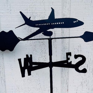 May include: Black metal airplane wind vane with a directional arrow and compass points. The airplane is facing right and the arrow is pointing left. The compass points are W, N, E, and S.
