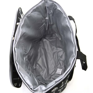 Może przedstawiać: Czarno-biała torba termoizolacyjna z zamkiem błyskawicznym i dwoma uchwytami. Torba jest otwarta, a wnętrze wyłożone jest srebrnym materiałem.