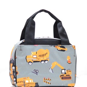 May include: A gray lunch bag with a black handle and a construction theme print. The print features yellow construction vehicles, including a cement mixer, an excavator, and a dump truck.