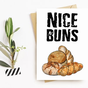 May include: A white card with black text that reads "NICE BUNS". The card features a drawing of various bread rolls, including a round bun with sesame seeds.