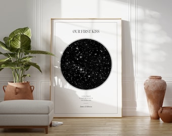 May include: A framed print with the text "OUR FIRST KISS" above a black and white star map. The print includes location and date details, with names at the bottom. The frame is gold, and the print is displayed on a wooden floor.